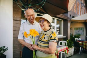 An older couple holding flowers in front of a restaurant.