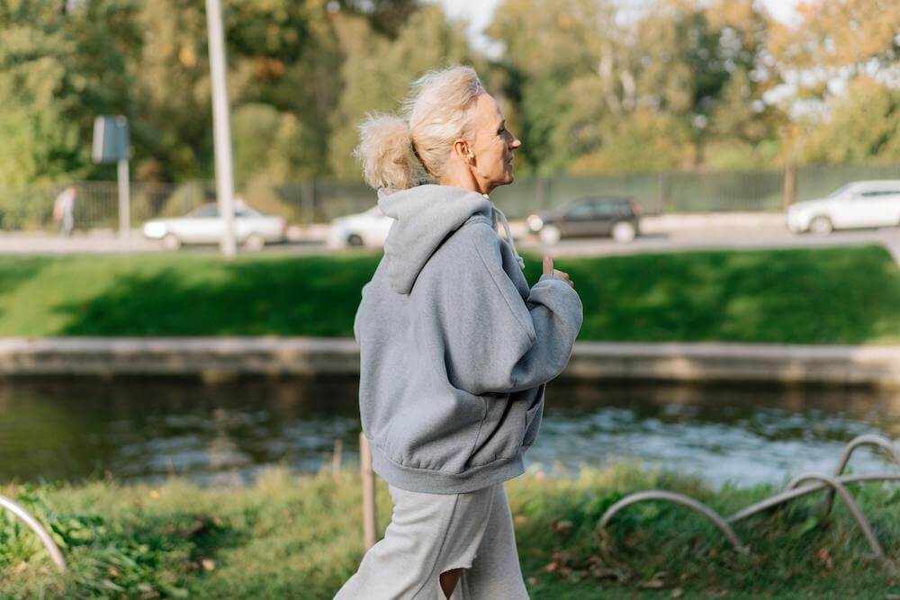 A woman in a gray hoodie walking by a river.