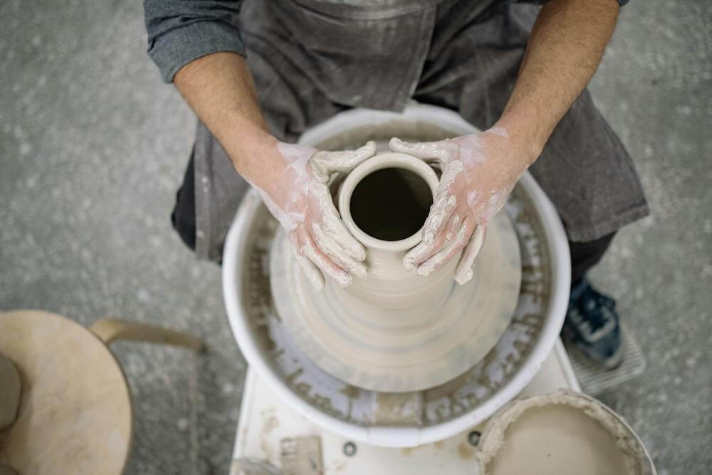 A senior man is engaged in social engagement while making a pot on a pottery wheel.