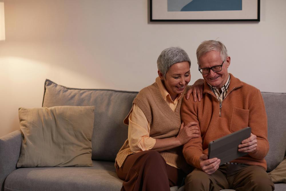 An older couple sitting on a couch looking at a tablet computer.