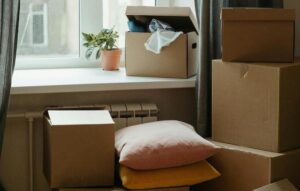 Photo of several moving boxes and a few pillows in front of a window.