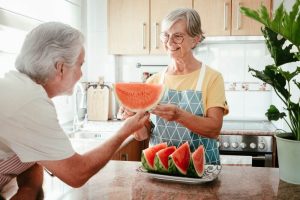Photo of an elderly couple in the kitchen eating water melon slices.
